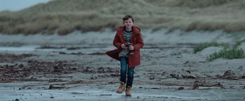 Movie still from “The Burning Sea” (2021), directed by John Andreas Andersen – A young boy is walking on the beach; Wide shot, Over the shoulder angle