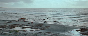 Movie still from “The Burning Sea” (2021), directed by John Andreas Andersen – A person standing on a beach near the ocean; Extreme Wide shot, High angle