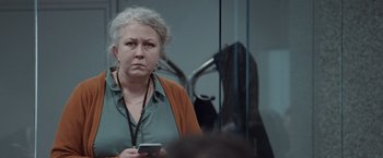 Movie still from “The Burning Sea” (2021), directed by John Andreas Andersen – An older woman holding a cell phone while standing in front of a mirror; Close Up shot, Over the shoulder angle