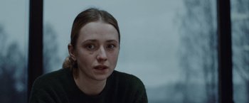 Movie still from “The Burning Sea” (2021), directed by John Andreas Andersen – A young woman with a bruised eye sitting in a room; Close Up shot, Over the shoulder angle