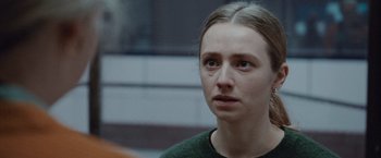 Movie still from “The Burning Sea” (2021), directed by John Andreas Andersen – A young woman looking at the camera while wearing a green shirt; Close Up shot, Over the shoulder angle