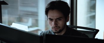 Movie still from “The Burning Sea” (2021), directed by John Andreas Andersen – A man looking at a computer screen while sitting in front of a window; Close Up shot, Low angle