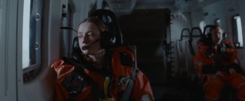Movie still from “The Burning Sea” (2021), directed by John Andreas Andersen – A person in a helicopter with a helmet on; Medium shot, Low angle
