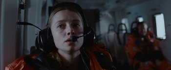 Movie still from “The Burning Sea” (2021), directed by John Andreas Andersen – A woman with a headset on in an airplane; Close Up shot, Low angle