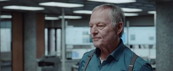 Movie still from “The Burning Sea” (2021), directed by John Andreas Andersen – An older man in a blue shirt is looking to his left; Close Up shot, Over the shoulder angle