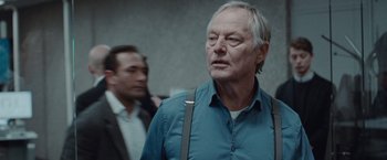 Movie still from “The Burning Sea” (2021), directed by John Andreas Andersen – An older man wearing a blue button up shirt; Close Up shot, Over the shoulder angle