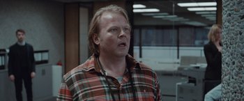 Movie still from “The Burning Sea” (2021), directed by John Andreas Andersen – A man in a plaid shirt is looking at the camera; Close Up shot, Over the shoulder angle