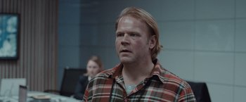 Movie still from “The Burning Sea” (2021), directed by John Andreas Andersen – A man with long blonde hair wearing a plaid shirt; Close Up shot, Over the shoulder angle