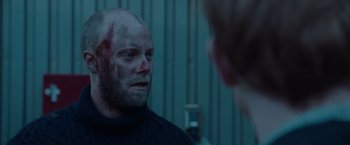 Movie still from “The Burning Sea” (2021), directed by John Andreas Andersen – A man with a shaved head is looking at another man with blood on his face; Close Up shot, Over the shoulder angle