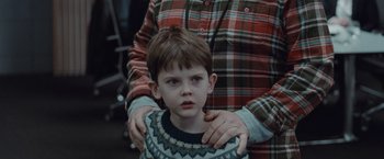 Movie still from “The Burning Sea” (2021), directed by John Andreas Andersen – A man holding a young boy in a plaid shirt; Close Up shot, Over the shoulder angle