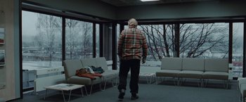 Movie still from “The Burning Sea” (2021), directed by John Andreas Andersen – An older man walking in a room with a lot of chairs; Wide shot, Over the shoulder angle