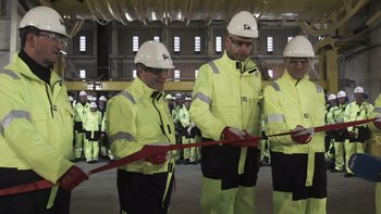 Movie still from “The Burning Sea” (2021), directed by John Andreas Andersen – A group of men in yellow jackets and hard hats cutting a red ribbon; Extreme Wide shot, Low angle