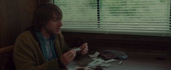 Movie still from “The Cabin in the Woods” (2011), directed by Drew Goddard – A man sitting in front of a table with a lot of cigarettes; Medium shot, High angle
