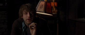 Movie still from “The Cabin in the Woods” (2011), directed by Drew Goddard – A young man holding a cell phone while sitting in front of a lamp; Close Up shot, Over the shoulder angle