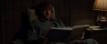 Movie still from “The Cabin in the Woods” (2011), directed by Drew Goddard – A man sitting in a chair looking at a book; Medium shot, High angle