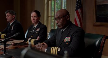 Movie still from “The Caine Mutiny Court-Martial” (2023), directed by William Friedkin – Two military men sitting at a table in front of american flags; Medium shot, Low angle