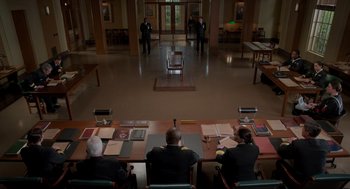 Movie still from “The Caine Mutiny Court-Martial” (2023), directed by William Friedkin – Three men sitting at a table in front of a door; Extreme Wide shot, High angle