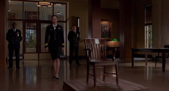 Movie still from “The Caine Mutiny Court-Martial” (2023), directed by William Friedkin – Two people in uniform walking in front of a wooden chair; Wide shot, Low angle