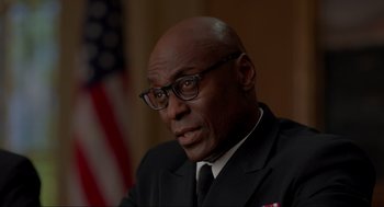 Movie still from “The Caine Mutiny Court-Martial” (2023), directed by William Friedkin – A man wearing a suit and glasses in front of an american flag; Close Up shot, Over the shoulder angle
