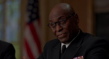 Movie still from “The Caine Mutiny Court-Martial” (2023), directed by William Friedkin – A man in a suit and tie with a flag in the background; Close Up shot, Over the shoulder angle