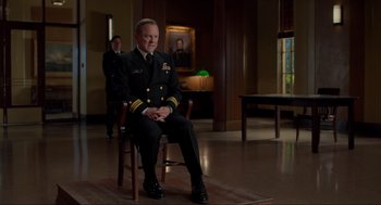 Movie still from “The Caine Mutiny Court-Martial” (2023), directed by William Friedkin – A man in uniform sitting on a chair in front of a window; Medium shot, Over the shoulder angle