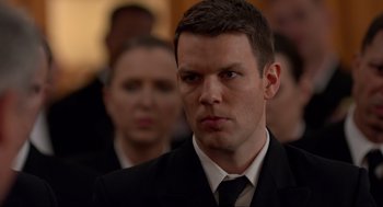 Movie still from “The Caine Mutiny Court-Martial” (2023), directed by William Friedkin – A man wearing a suit and tie in front of a group of people; Close Up shot, Over the shoulder angle