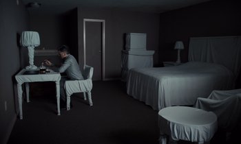 Movie still from “The Card Counter” (2021), directed by Paul Schrader – A man sitting at a table in a room with two beds; Wide shot, High angle