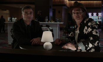 Movie still from “The Card Counter” (2021), directed by Paul Schrader – Two men sitting at a table in front of a lamp; Medium shot, Low angle