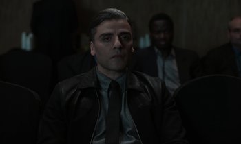 Movie still from “The Card Counter” (2021), directed by Paul Schrader – A man in a suit and tie sitting in front of other men; Close Up shot, Over the shoulder angle