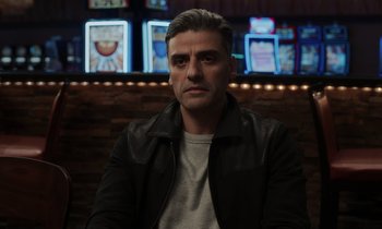 Movie still from “The Card Counter” (2021), directed by Paul Schrader – A man sitting in front of a wall with lights behind him; Close Up shot, Over the shoulder angle