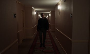 Movie still from “The Card Counter” (2021), directed by Paul Schrader – A man standing in a long hallway in a hotel; Wide shot, Low angle