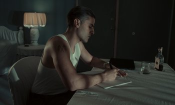 Movie still from “The Card Counter” (2021), directed by Paul Schrader – A man sitting on a bed writing on a book; Medium shot, High angle