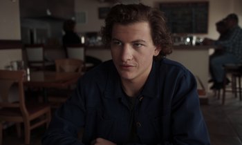 Movie still from “The Card Counter” (2021), directed by Paul Schrader – A man with curly brown hair sitting at a table; Close Up shot, Low angle