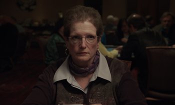 Movie still from “The Card Counter” (2021), directed by Paul Schrader – An older woman wearing glasses sitting in front of a group of people; Close Up shot, Over the shoulder angle