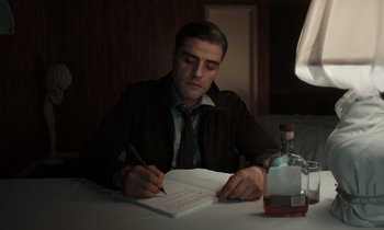 Movie still from “The Card Counter” (2021), directed by Paul Schrader – A man sitting at a table writing on a piece of paper; Medium shot, Low angle
