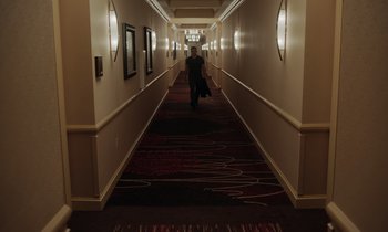 Movie still from “The Card Counter” (2021), directed by Paul Schrader – A person walking down a long hallway in a hotel; Wide shot, High angle