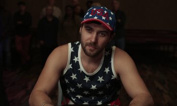 Movie still from “The Card Counter” (2021), directed by Paul Schrader – A man wearing a red , white and blue hat; Medium shot, High angle
