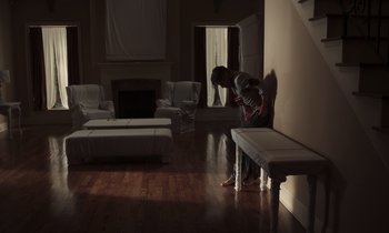 Movie still from “The Card Counter” (2021), directed by Paul Schrader – A person standing in a room with a fireplace; Wide shot, Low angle