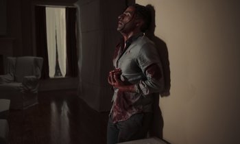 Movie still from “The Card Counter” (2021), directed by Paul Schrader – A man with a bloody shirt on standing in a room; Wide shot, Low angle