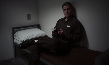 Movie still from “The Card Counter” (2021), directed by Paul Schrader – A man sitting on a bed holding a cell phone; Medium shot, Low angle