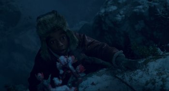 Movie still from “The Christmas Chronicles: Part Two” (2020), directed by Chris Columbus – A young person wearing a winter coat and a fur hat is laying on the ground in the dark; Close Up shot, High angle