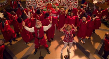 Movie still from “The Christmas Chronicles: Part Two” (2020), directed by Chris Columbus – A group of people dressed in red singing; Extreme Wide shot, High angle