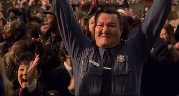 Movie still from “The Christmas Chronicles: Part Two” (2020), directed by Chris Columbus – A man in a police uniform raises his arms in the air; Close Up shot, High angle