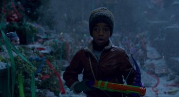 Movie still from “The Christmas Chronicles: Part Two” (2020), directed by Chris Columbus – A young boy in a brown jacket holding a toy gun; Medium shot, High angle