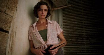 Movie still from “Crimes of the Future” (2022), directed by David Cronenberg – A woman leaning against a wall with a book in her hand; Medium shot, High angle