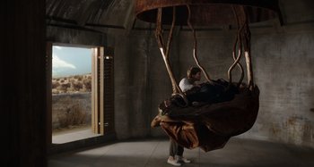 Movie still from “Crimes of the Future” (2022), directed by David Cronenberg – A man standing next to a tree in a room; Wide shot, Low angle