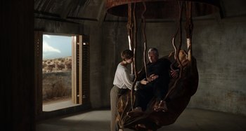 Movie still from “Crimes of the Future” (2022), directed by David Cronenberg – A man and a woman sitting on a swing; Wide shot, Low angle