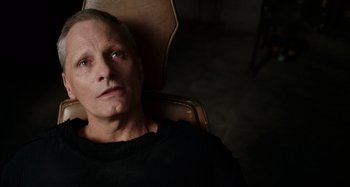 Movie still from “Crimes of the Future” (2022), directed by David Cronenberg – A man sitting in a chair looking at the camera; Close Up shot, High angle