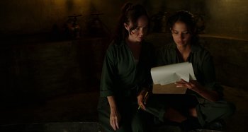 Movie still from “Crimes of the Future” (2022), directed by David Cronenberg – Two women sitting on the ground looking at a piece of paper; Medium shot, Over the shoulder angle