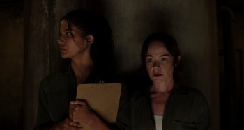 Movie still from “Crimes of the Future” (2022), directed by David Cronenberg – Two women are standing next to each other holding a clipboard; Medium shot, Low angle